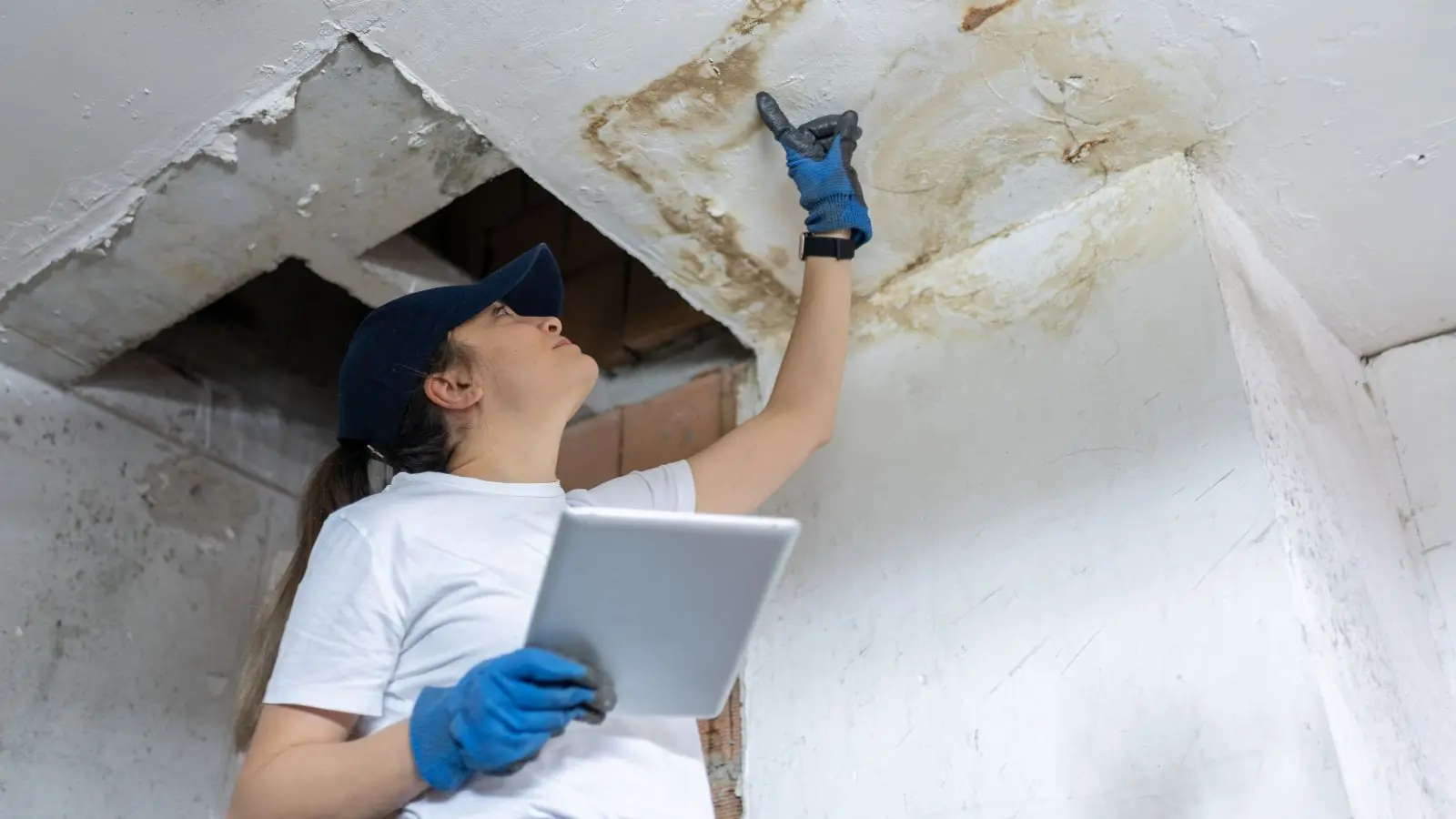 Inspector with a tablet looking at a water-stained ceiling opening