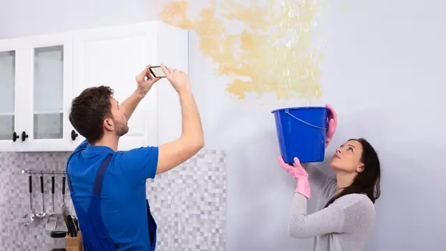 Couple photographing a water stain on a wall while holding a bucket